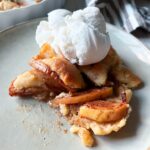 Närbild på äppelpaj med kolakakssmul, kanelstekta äpplen och vaniljglass på ett fat