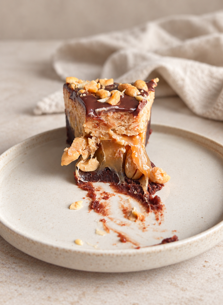 Snickerskladdkaka med chokladganache, jordnötter och seg kola på en beige tallrik